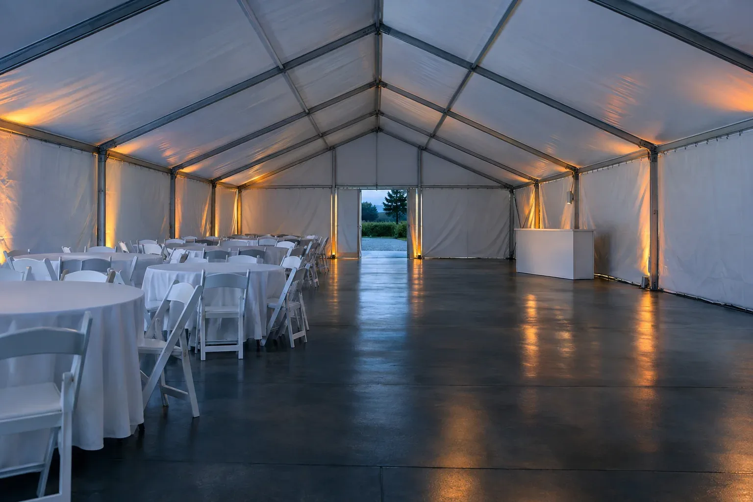 Inside an empty frame tent, round tables and chairs on one half, open floor and a small bar on the other, a clear aisle between them