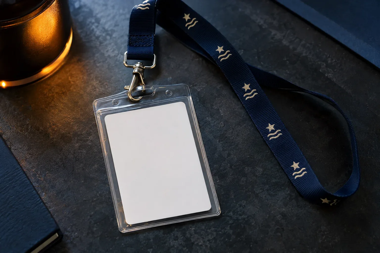 A blank white card in a clear holder clipped to a navy lanyard printed with a cream star and wave mark, on dark slate