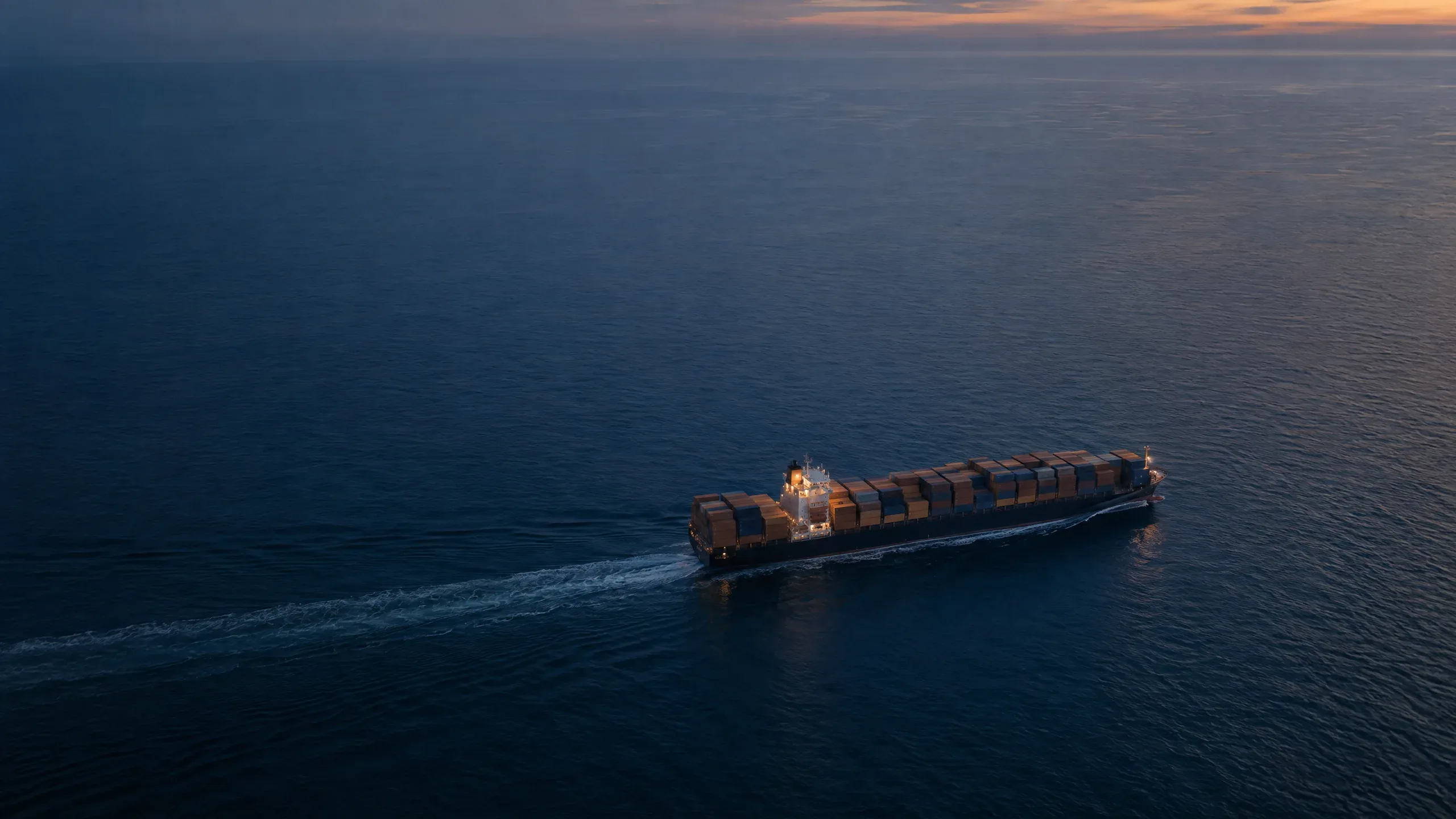 A loaded container ship at sea at dusk, seen from above