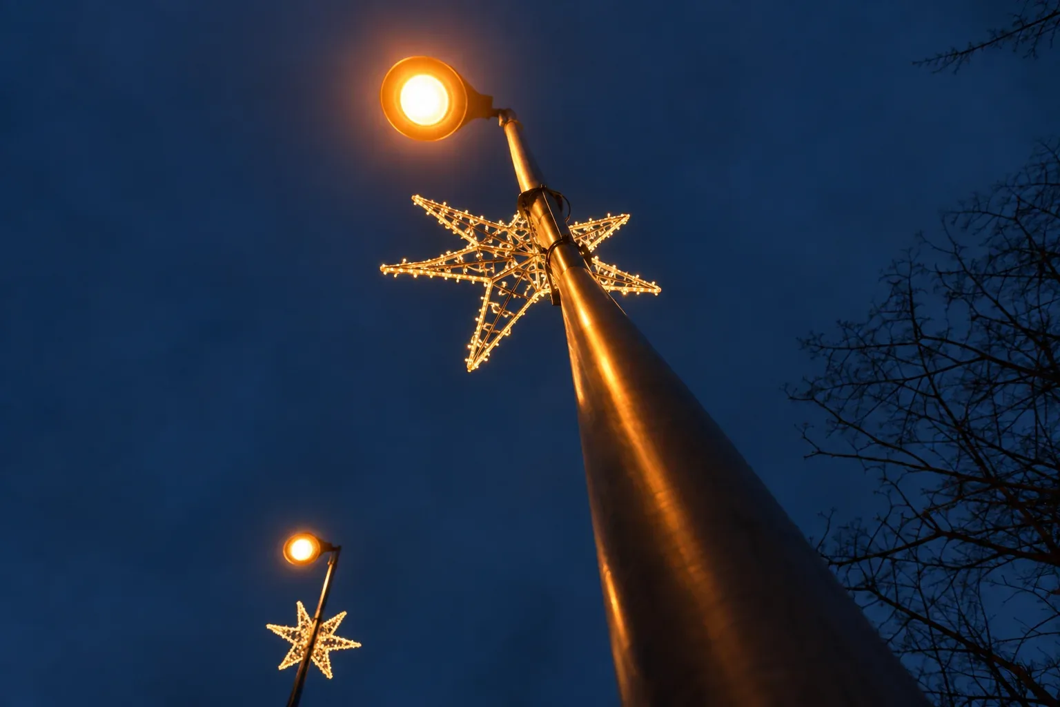Looking up a street-light pole at a lit star decoration against the night sky