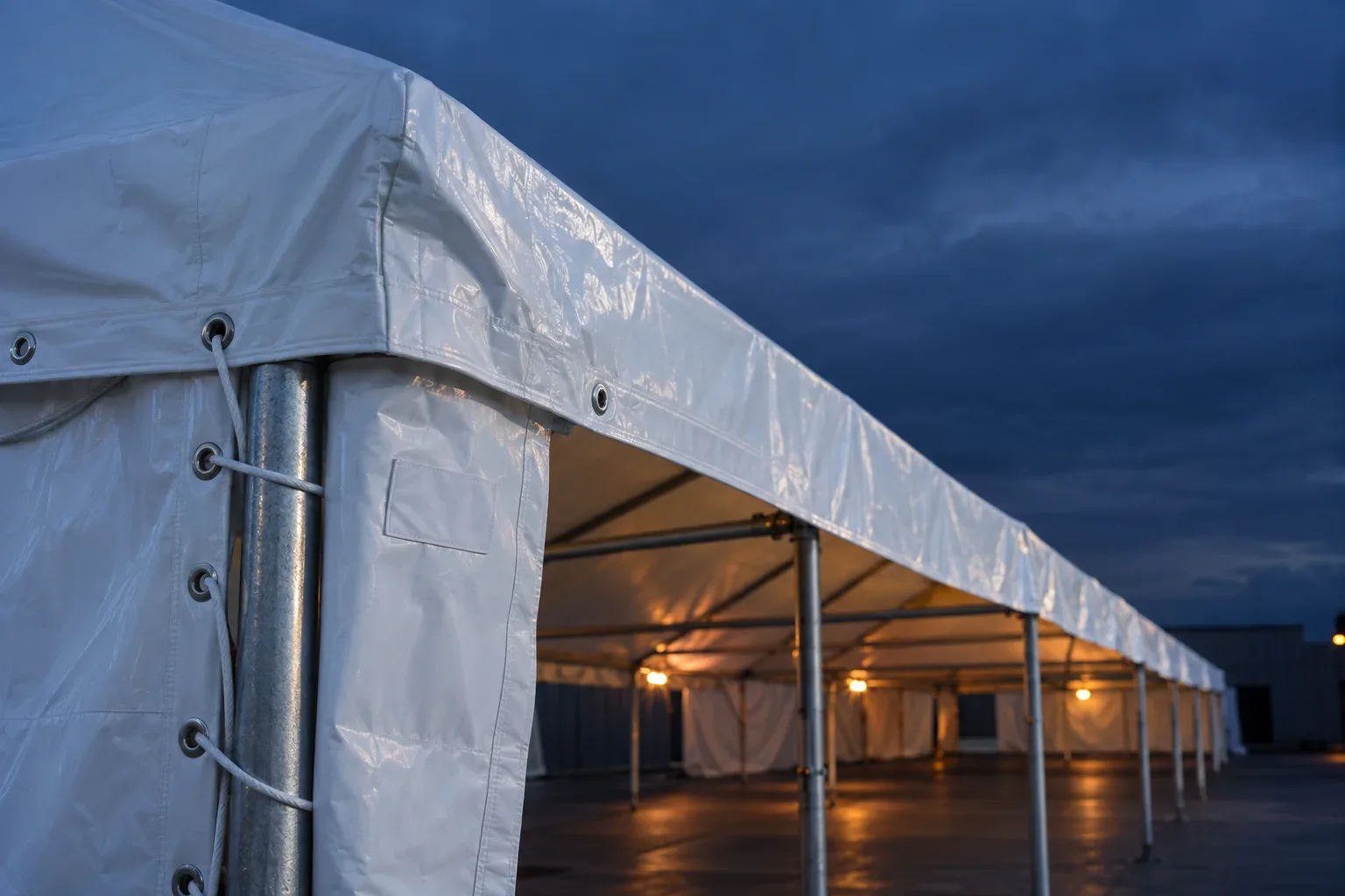Close-up of a white PVC tent top and sidewall laced to a galvanized leg, with welded seams, grommets and a blank label patch