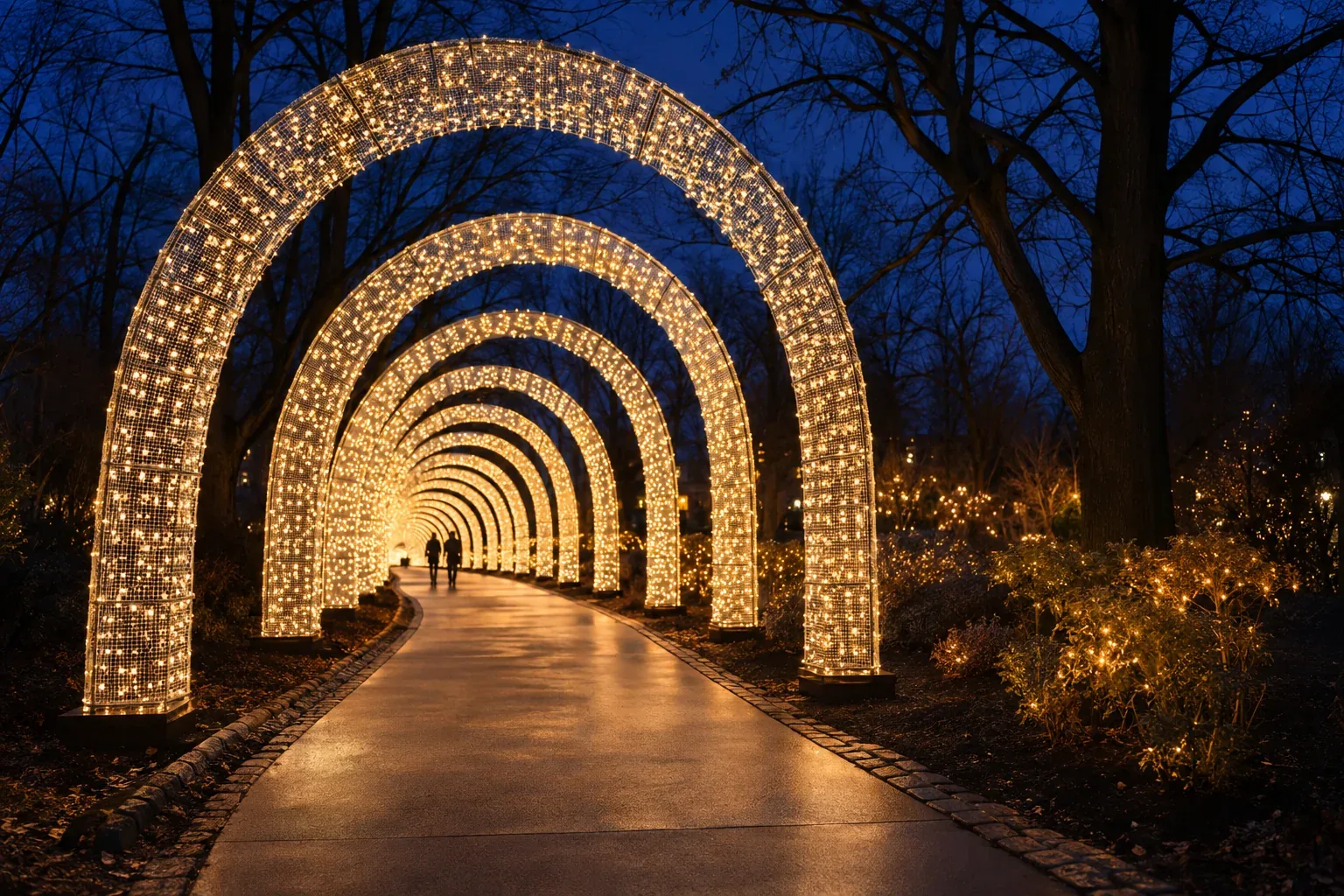 A long tunnel of lit arches over a curving park path at night